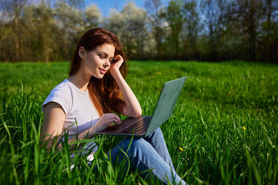 Young woman using laptop while sitting on field