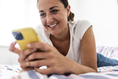 Smiling woman using smart phone on bed at home