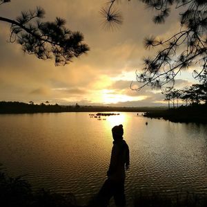 Silhouette man standing by lake against sky during sunset