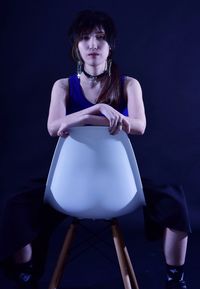 Portrait of young woman on seat against black background