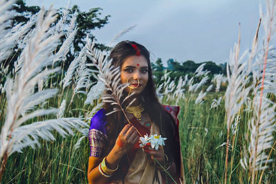 Portrait of young woman wearing sari holding plant on land