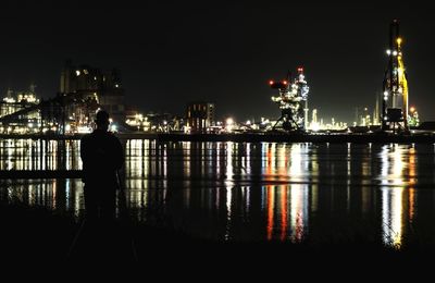 Illuminated buildings by river against sky at night