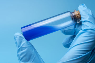 Close-up of person holding bottle against blue background