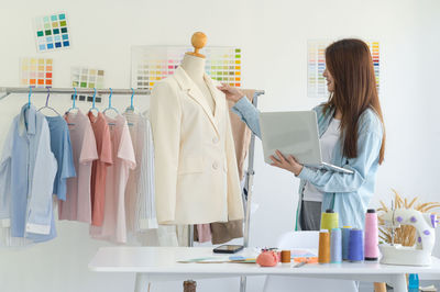 Young female tailor designer working with a tailor dummy and laptop in a workshop.