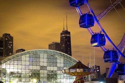 Illuminated ferris wheel against buildings in city