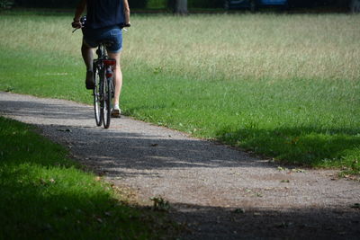 Low section of woman riding bicycle by field on road