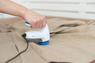 Woman uses a machine for removing pellet and spools from clothes and fabric on black trousers.