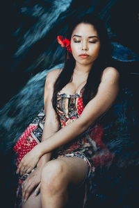 Young woman with eyes closed sitting against waterfall