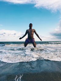 Full length of shirtless man in sea against sky