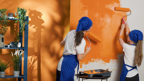 Rear view of mother and daughter standing against wall