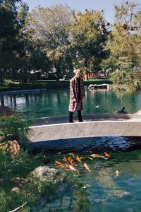 Man standing on footbridge over lake with fishes against trees