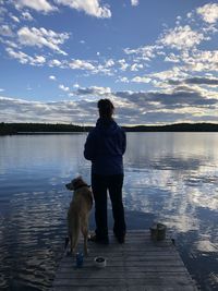 Rear view of dog standing on lake against sky