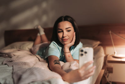 Young woman using mobile phone while lying on bed at home