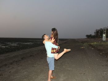 Young couple standing on beach against clear sky