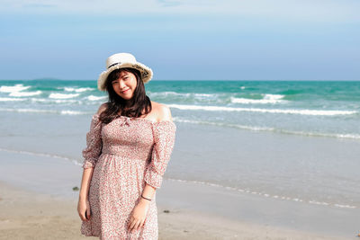 Young woman standing at beach against sky