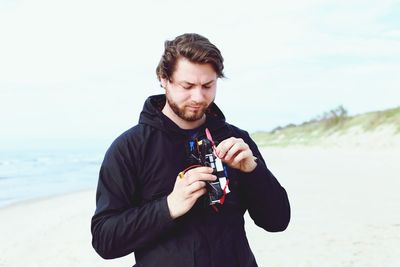 Man holding quadcopter while standing at beach