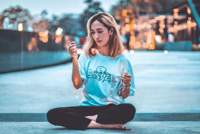 Beautiful young woman sitting on street in city