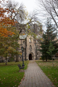 Footpath amidst trees and buildings against sky during autumn