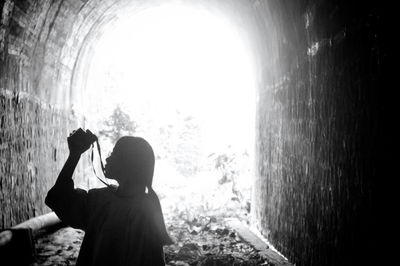 Side view of woman photographing while standing in tunnel