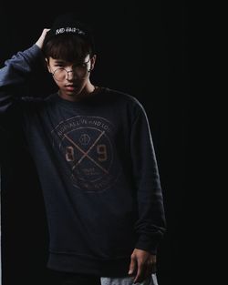 Portrait of young man standing against black background