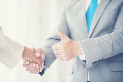 Midsection of businessman shaking hands with colleague while showing thumbs up