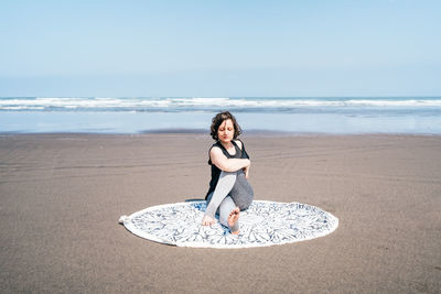 Full body young female in sportswear doing half lord of the fishes variation while practicing yoga on sandy seashore with eyes closed