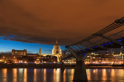 Illuminated bridge over river with buildings in background at night