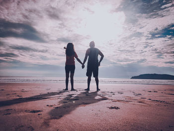 Full length of friends standing on beach against sky during sunset