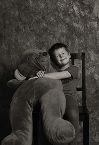 Boy with stuffed toy sitting on chair against wall