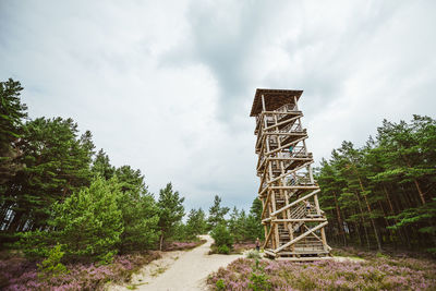 Lookout tower amidst trees against cloudy sky