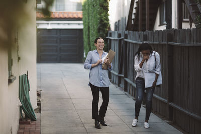 Female designers discussing while walking on sidewalk by building against sky