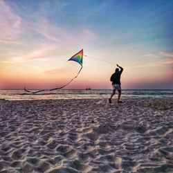 Woman flying kite at beach against sky during dusk