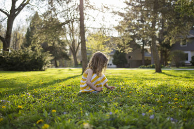 Girl picking flowers while crouching in backyard