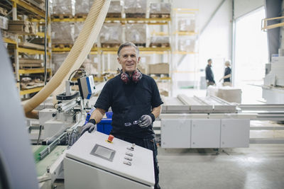 Portrait of smiling senior worker standing by machine at industry