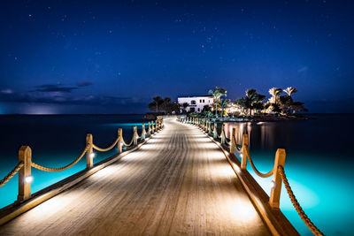 Illuminated pier over sea against sky at night