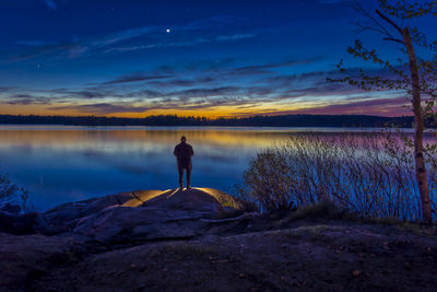 Rear view of silhouette man standing by lake against sky during sunset