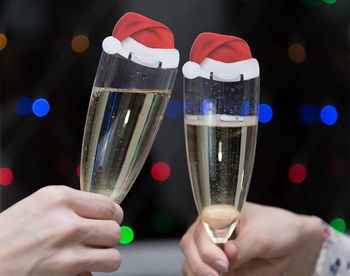 Cropped hands of friends toasting champagne flutes with santa hats