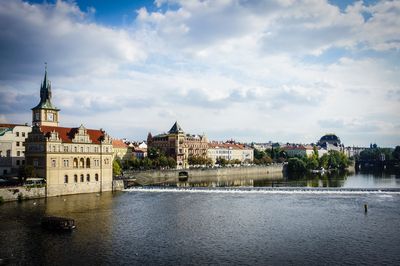 Buildings at waterfront against cloudy sky