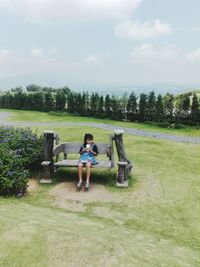 Full length of man sitting on field against sky