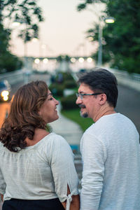 Rear view of couple looking at each other while standing in city during sunset