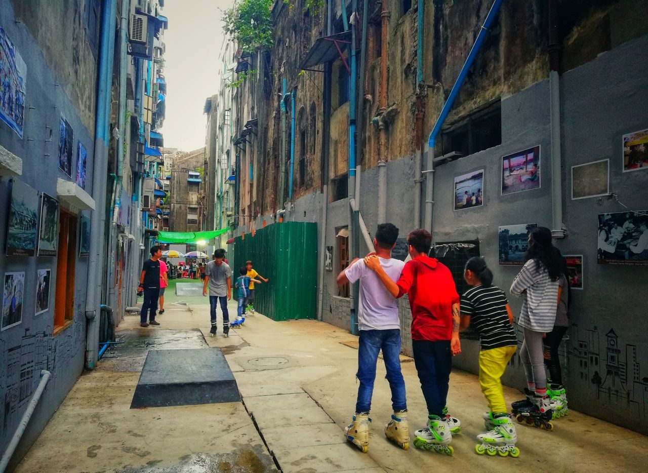 architecture, building exterior, built structure, real people, group of people, city, men, building, full length, lifestyles, child, people, women, street, residential district, day, rear view, medium group of people, group, city life, outdoors, alley, teenager