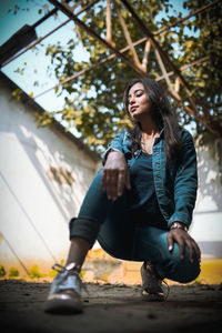 Young woman looking away while sitting on tree