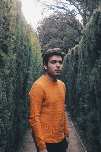 Portrait of young man standing by tree in forest