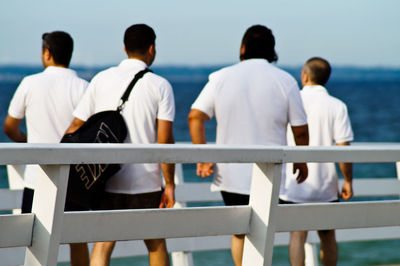 Rear view of friends walking on pier against sea