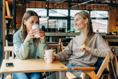 Two attractive women are discussing and drinking coffee in a coffee shop.