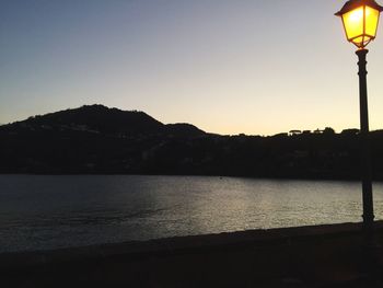 Silhouette street light by lake against sky during sunset