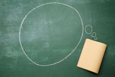 Directly above shot of blank speech bubble with book on blackboard