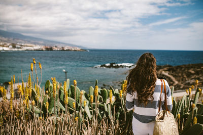 Rear view of woman standing by sea against sky