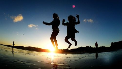 Silhouette children jumping at beach against sky during sunset