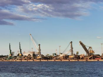 Cranes at harbor against sky